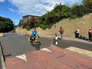 Photograph of a woman, Sophie Walker, riding a loaded yellow bike cycling down a road with red tarmac.
