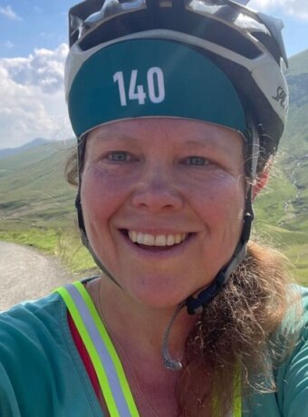A selfie photograph of a smiling woman, Sophie Walker, with the background of valley up to Newlands Pass.