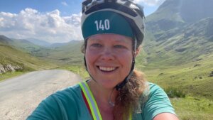 A selfie photograph of a smiling woman, Sophie Walker, with the background of valley up to Newlands Pass.